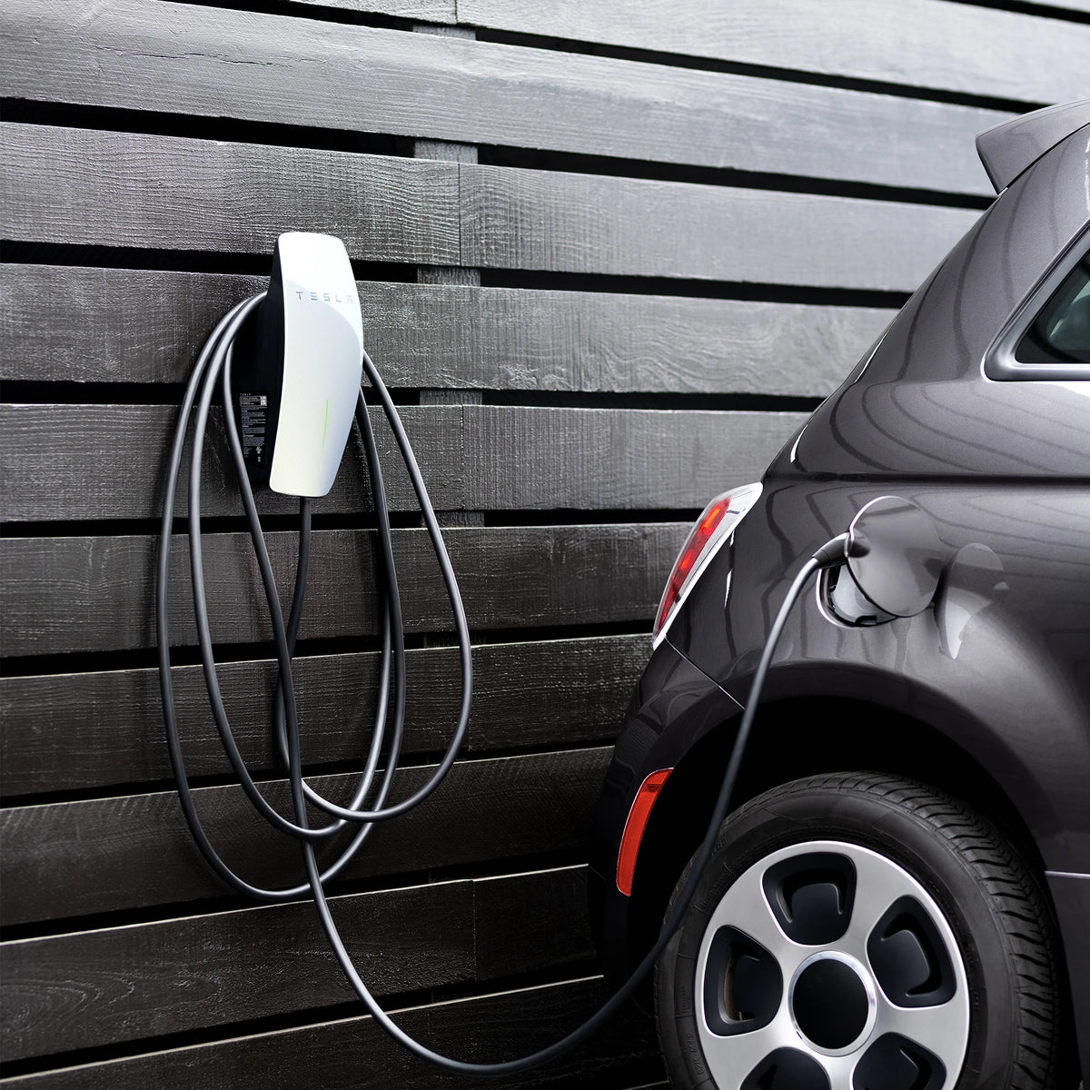 Tesla Wall Connector aan een houten gevel, laadt een auto van een ander merk