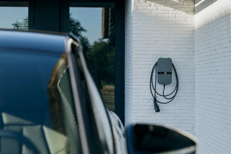 Peblar-laadpaal met kabel aan een witte gevel bij de oprit